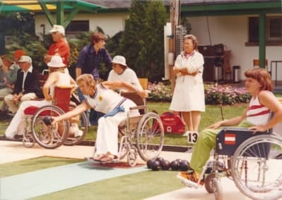 Women wheelchair athletes playing bowls. Umpire to the back of them.