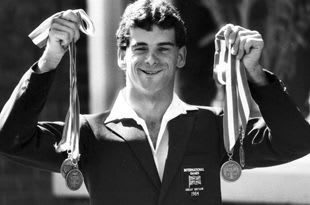 Black and white image of Paralympian, Tony Griffin, holding up some of his winning medals