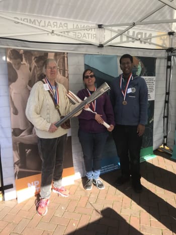Three of the volunteers from I have a voice too standing in the pop-up museum holding Paralympic torches