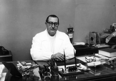 Black and white photo of Dr Antonio Maglio in Doctors white coat sat behind his desk