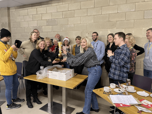 Members from the NPHT Team around a desk opening the box with Adam Hills gold prosthetic foot.