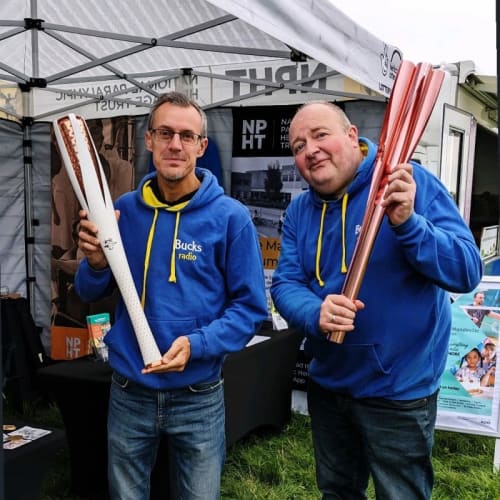 Two men holding Paralympic torches outside the entrance of the Pop-up museum tent.