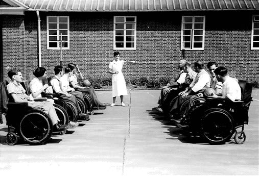 Physiotherapist and patients in wheelchairs outside with medicine balls